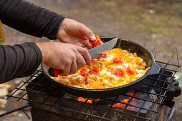A man slices tomatoes in order to fry them with eggs