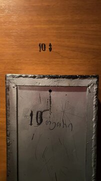 Vertical 4K video. Fare payment. Female hand puts silver coin into old metal acceptor. Woman in wooden elevator presses number six and push door close button. Translation from Georgian: 10 tetri