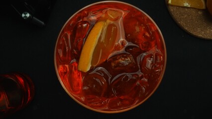 Macrography, experience the art of decorate a Negroni cocktail from a top-down perspective, adorned with a fresh vibrant orange slice, all against a dramatic black background. Alcoholic. Comestible.