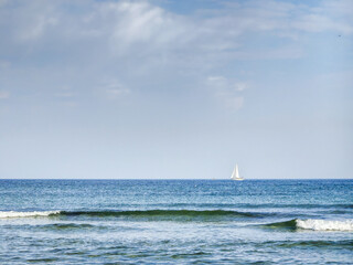 Fototapeta premium Lonely sailboat on the empty sea, cloudy sky during morning hours