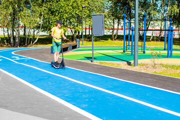 12 year old boy riding scooter on bike path in park in summer