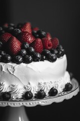A white cake with blueberries and strawberries on top. The cake is decorated with whipped cream and strawberries