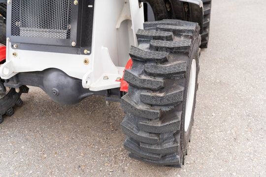 A detailed closeup view of an oversized agricultural tractor tire positioned on a rough gravel surface, showcasing its rugged design and durability