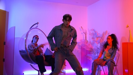 Fototapeta premium Skilled asian dancer moving to modern music while multicultural friend sitting at chair. Professional performer dancing show energetic foot step while hipster team cheering and supporting. Regalement.