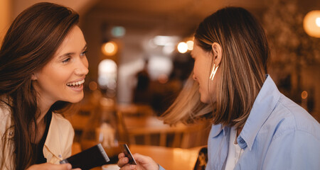 Photo of good looking young women in summer clothing, spend spare time together, watch photo card, nostalgia rest in restaurant. Two girls sisters laughing, have a good time.