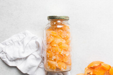 Overhead view of tangerine cheong in a glass jar on a white background, top view of korean tangerine cheong in a transparent jar, tangerine in sugar syrup, process of making tangerine cheong