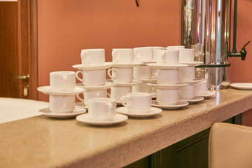 There is a neat stack of coffee cups and matching saucers placed on a counter
