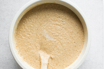Overhead of moi moi mixture in a white ceramic bowl, top view of nigerian bean pudding being mixed, process of making nigerian moi moi