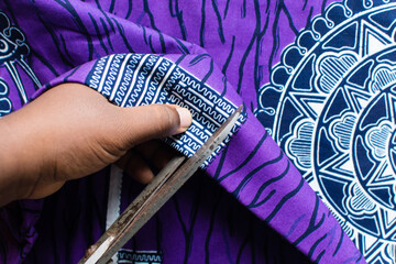 top view of cutting ankara fabric with scissors , flatlay of nigerian wax print cloth, rumpled...