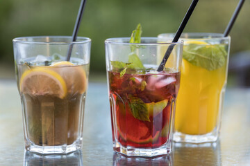 Three glasses of different colored drinks with straws in them