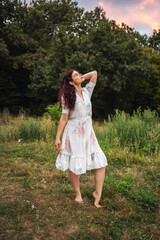 Retro style. Young beautiful girl with black chic hair in a white dress on the background of a forest and a red sunset.