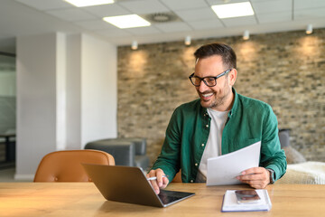 Portrait of handsome manager analyzing financial reports over computer at his workplace in modern...