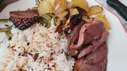Assiette composé de magret de canard avec accompagnement dont riz, pommes de terre et cornichons...