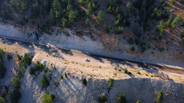 A white car parked on a high hillside on an empty highland road among pine trees and wild bushes. Aerial view at G&ouml;mbe Plateau of Kaş, Antalya in Turkey