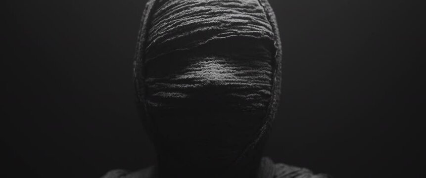 A mummy of a woman against the dark background looks around 