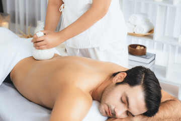 Hot herbal ball spa massage body treatment, masseur gently compresses herb bag on man body....