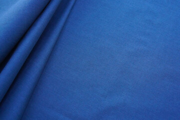 Blue cotton fabric background. Navy blue plain textile template with neat folds on the left side, copy space, perspective view, selective focus. Backdrop with monochromatic denim material.