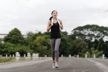 Confident Runner:  A young woman in athletic wear runs with determination on a paved road, showcasing a healthy lifestyle and fitness goals.  Her confident stride and bright smile evoke a sense of ene