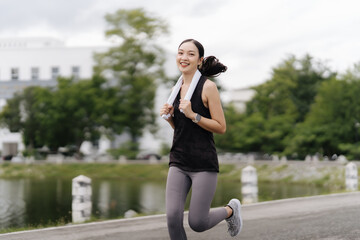 Urban Runner's High: A young Asian woman beams with exhilaration while jogging in the city, towel...