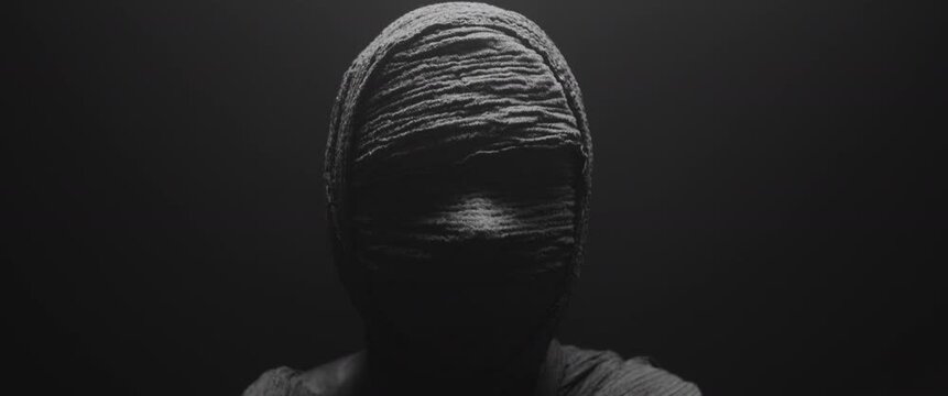 A mummy of a woman against the dark background raises her head and looks around 