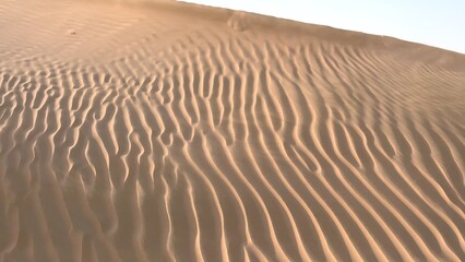 Sand patterns become more defined as evening light fades, casting soft shadows across desert. Intricate texture of dunes is highlighted by warm glow of dusk, showcasing natural beauty.