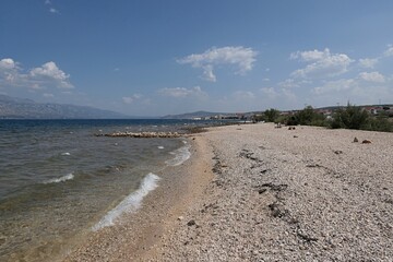 Empty rocky summer beach, bay north of Razanac town, Zadar district, northern Dalmatia, Croatia. End of august 2024 season, clear skies with some cumulus clouds in distance.