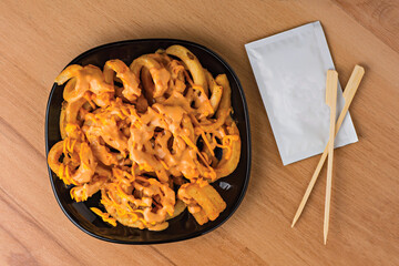 Loaded Curly Fries with Cheesy Sauce and Dipping Sauce served in plate isolated on wooden table top view fast food snacks