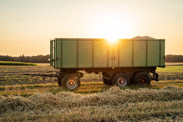 Obraz premium Getreideernte - Transportanhänger auf dem Getreidefeld im Gegenlicht der untergehenden Sonne.