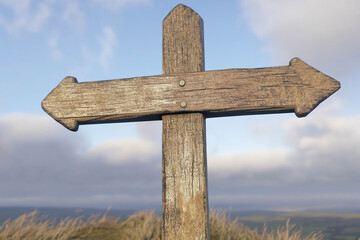 A weathered wooden signpost in the shape of a cross, with a single blank arrow pointing to the right, stands on a hilltop against a cloudy sky. Generated with AI.