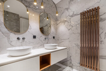 A luxurious bathroom decorated with white marble tiles. The battery is copper color. .Stylish lamps...