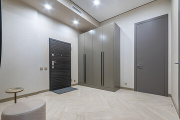 Modern design of the hallway, decorated in light beige color. Black front door, .grey wardrobe.