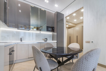 Kitchen in a modern apartment. Stylish design of the kitchen set with built-in appliances. Dining table with upholstered chairs.