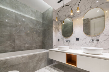 Spacious bathroom with an exclusive design. The room is decorated with white and gray marble tiles....