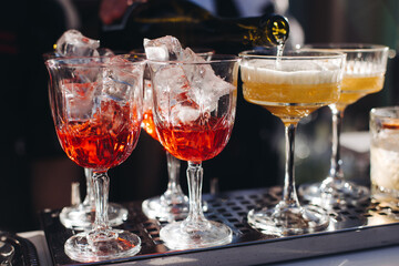 Bartender working, beautiful row line of different coloured liquor alcohol cocktails on a open air party in a bar, and others on catering banquet on event, barman mixing drinks and beverages in club