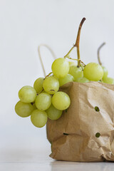 Bunch of fresh green grapes in recyclable paper bag. Cluster of grapes in eco-friendly packaging on white background. Copy space.