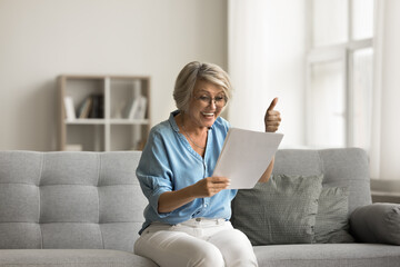 Overjoyed older woman at home read letter and showing thumbs-up gesture, smile, get happy news,...