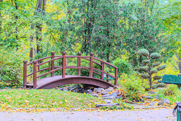 Park bridge. Yellow, orange and red autumn leaves on ground in beautiful fall park. Fallen golden autumn leaves on green grass in sunny morning light yard, toned photo. Fall park landscape background