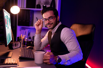 Profile in smart businessman wearing glasses remotely working on desk, looking at camera with waistcoat costume, presenting professional meeting online marketing at neon dark lighting office. Surmise.