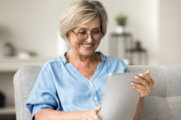 Attractive middle-aged woman using digital tablet, reading social media news, browsing wireless internet, connecting with family friends by messages, watching on-line videos Modern technology, leisure