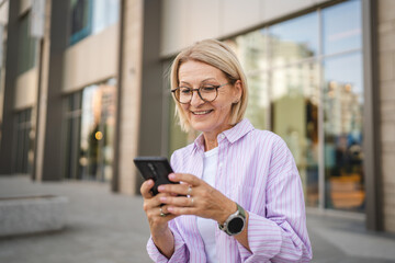 Fototapeta premium Happy mature woman sit and use mobile phone on the street