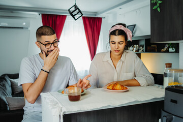 Two friends male and female are eating croissant for breakfast