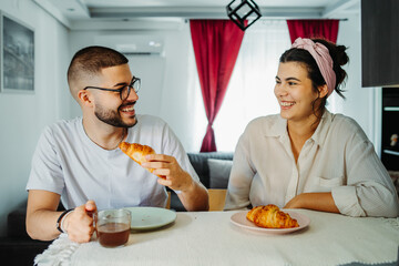 Two friends male and female are eating croissant for breakfast