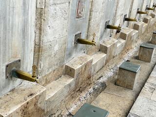 Historical stone water fountains with brass taps and stone basins for ceremonial washing at an ancient site.