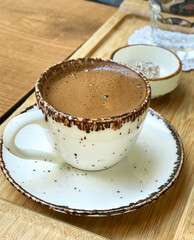 Close-up of a freshly brewed cup of Turkish coffee being prepared, showcasing rich aroma and traditional ceramic cup on a wooden table