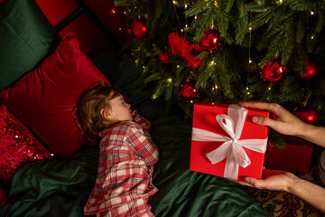 Little girl sleeps by the Christmas tree waiting for Santa Claus. Child peacefully sleeps on...