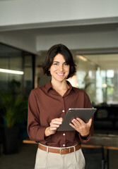 Smiling young Hispanic professional business woman using tablet standing in office. Happy...