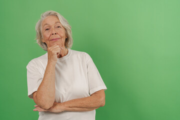 An older woman is joyfully smiling and posing in a thoughtful manner against a vibrant green screen backdrop
