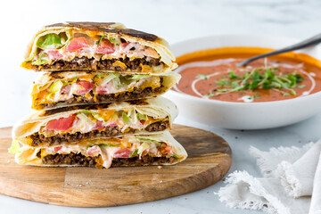 A stack of homemade crunch wraps with roasted red pepper soup in behind.