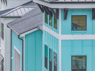 Aerial close up view of modern apartment condo building roof with dark brown gutter system, turquoise vinyl siding, square windows with brown metal frames  