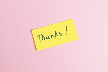 Yellow small note with the word thank you on a pink background in the center